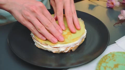 Female hands assembling layered pancake cake indoors on table Stock Footage 342880587