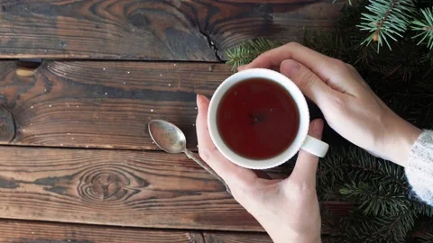 Female hands bask about a cup of hot tea on a wooden table with fir branches Stock Footage 140808560