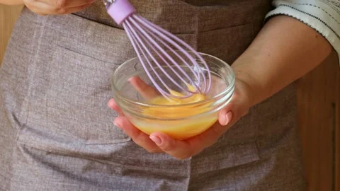 Female hands beating eggs with a whisk in a bowl to prepare dough Stock Footage 285776092