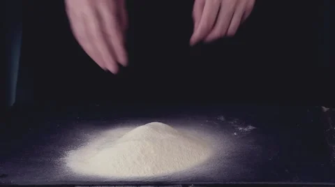Female hands break the egg into flour for making dough over black table. Dark Stock Footage 59859367