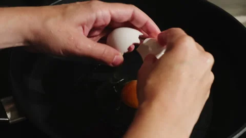 Female hands breaking egg to cook fried eggs in a pan Stock Footage 340331492
