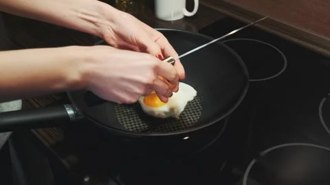 Female hands breaking eggs and frying on black electric cooktop indoors Stock Footage 340879836