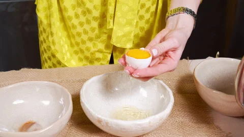 Female hands breaking eggshells dividing yolks and whites into different bowls Stock Footage 153696409