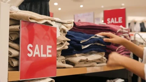 Female Hands Choosing Jeans from Stack in Clothing Store. Big Red Sign in Stock Footage 82106108
