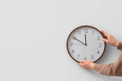 Female hands with clock on light wall. Daylight saving time concept Stock Photos