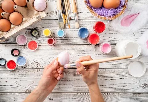 Female hands coloring easter eggs with pastel paints, top view flat lay Stock Photos