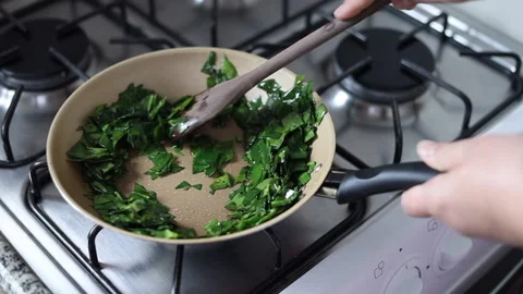 Female hands cooking ora-pro-nobis in frying pan. Stirring wooden spoon Stock Footage 196848754