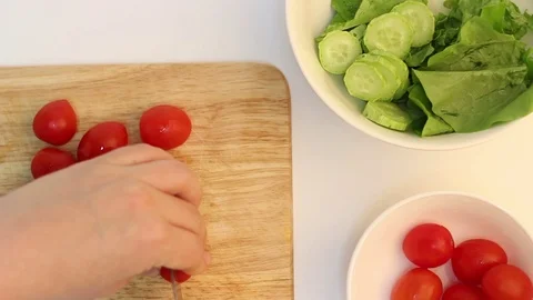 Female hands cut cherry tomatoes on a wooden board with knife, top view Stock Footage 122305680