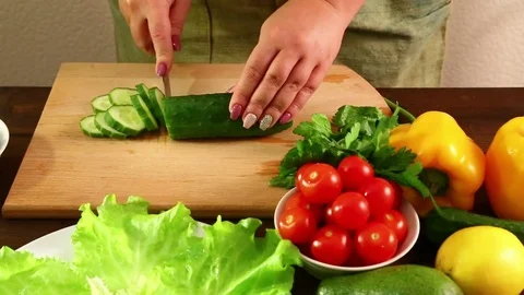 Female hands cut a cucumber to make a vegetable salad. Stock Footage 80400314