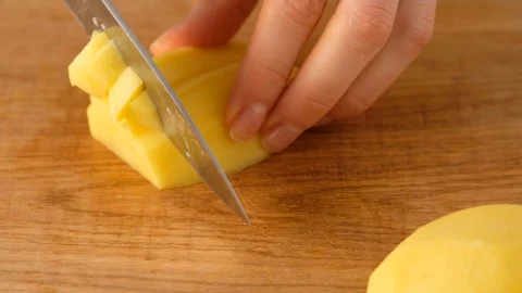 Female hands cut raw potatoes with a knife on a wooden board. Potato slicing Stock Footage 129694444