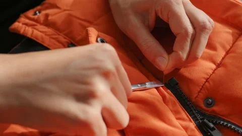 Female hands cuts the thread with scissors on orange waterproof fabric of winter Видео 220660479