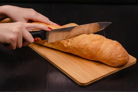 Female hands cutting bread on a cutting board on a wood background Stock Photos