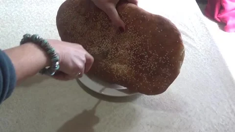 Female hands cutting oval bread with sesame seeds into two parts Video stock 307756408