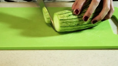 Female hands cutting vegetable marrow into slices on plastic cutting board. HD Video stock 70933774
