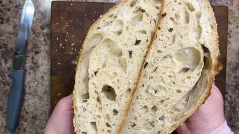 Female hands demonstrate two halves of freshly cut sourdough bread. 스톡 동영상 344188128