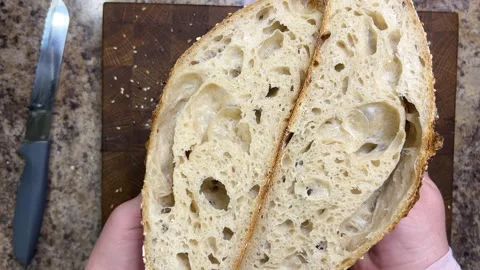Female hands demonstrate two halves of freshly cut sourdough bread. Video stock 344188450