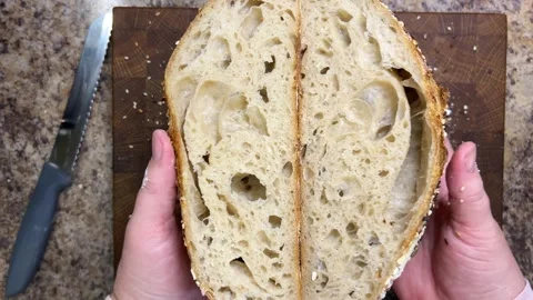 Female hands demonstrate two halves of freshly cut sourdough bread. Video stock 344189315