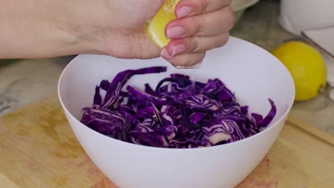 Female hands dressing red cabbage salad with lemon juice in a white bowl Stock Footage 297014777
