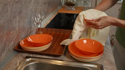 Female hands drying orange ceramic dishes after washing. Soft towel removes Stock-Footage 316755063