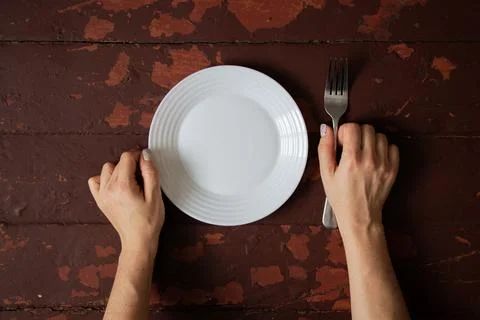Female hands with fork and empty plate on old wooden table, concept of hung.. Stock-Fotos