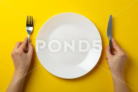 Female Hands Hold Fork And Knife On Yellow Background With Plate, Top View