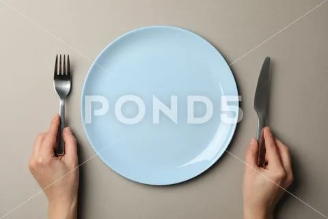 Female hands hold fork and knife on grey craft background with plate, top vie Stock-Fotos