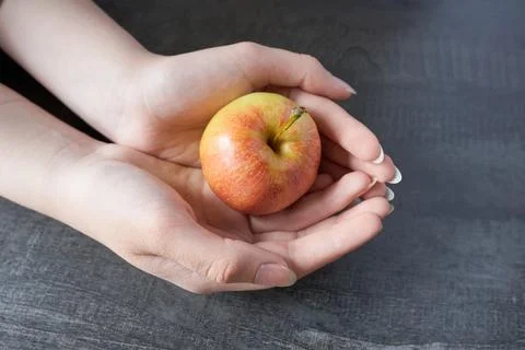 Female hands hold a red apple on a dark wooden background. Close-up. Stock Photos