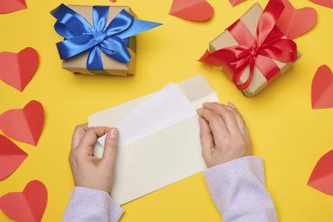 Female hands hold a white rectangular envelope on a yellow background, paper red Stock Photos