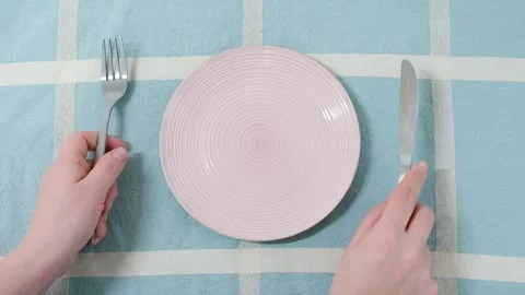 Female hands holding a fork and and knife next to an empty pink plate on a blue Stock Footage 264196616