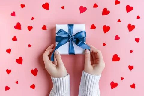 Female Hands holding a gift in white wrapping paper on pink background with red Stock Photos