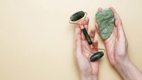 Female hands holding marble face roller and gua sha tools for skincare routin Stock Photos