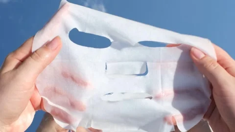 Female hands holding a mask sheet on blue sky and clouds background close-up. Video stock 340956775
