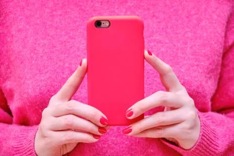 Female hands holding the phone in a red case. The girl holds the phone and ta Stock Photos