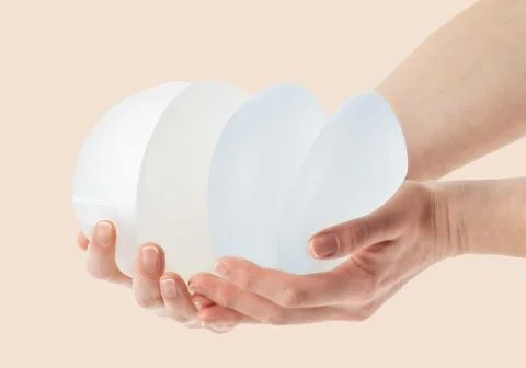 Female hands holding stack of different types of breast implants. Stock Photos