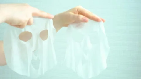 Female hands holding two moisturizing mask sheets on gray background close-up. Stock Footage 305018849