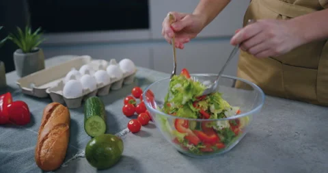 Female hands holding two spoons and mixing vegetable salad in transparent bowl Stock Footage 148746621