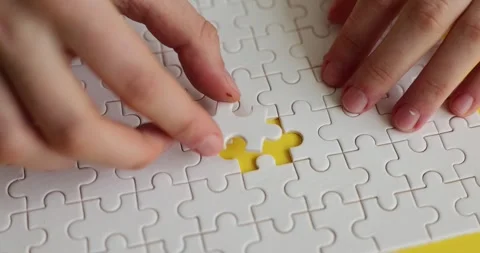 Female hands insert missing piece into white puzzle on table Stock Footage 241222274