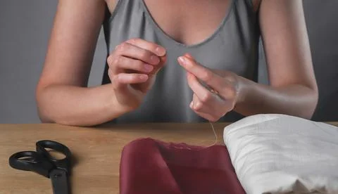 Female hands inserting thread through tiny needle hole for sewing Foto stock