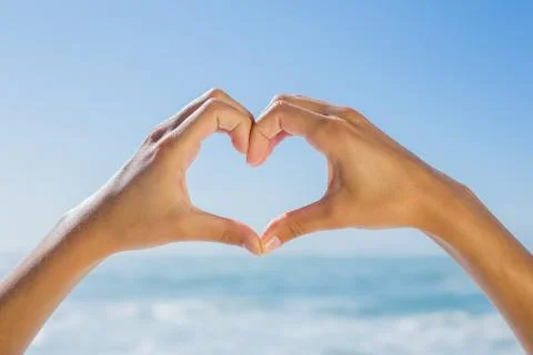 Female hands making heart shape by the sea Stock Photos