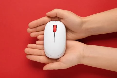Female hands with modern wireless computer mouse on red background Foto stock