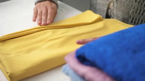 Female hands neatly stack yellow dress in pile with ironed clothes. Girl ironing Stock Footage 131225297