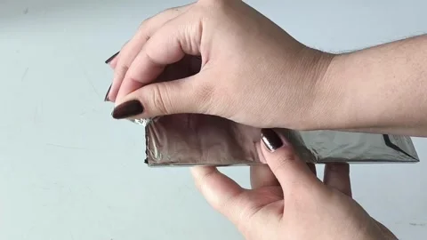 Female hands opening a package of chocolate foil. Dark chocolate in foil Stock Footage 330156717