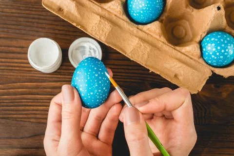 Female hands painted blue Easter eggs with a brush, top view 库存照片