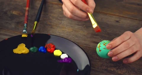 Female hands painting on Easter eggs on wooden background with palette. Natural Stock Footage 150955727