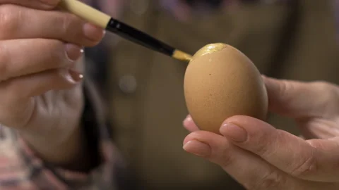 Female hands painting eggs using brush with gold paint. Easter, tradition and Stock Footage 329090073