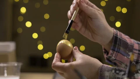 Female hands painting eggs using brush with gold paint with festive garland Stock Footage 329090127