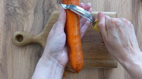 Female hands peeling a raw orange carrot with a manual tool Stock Footage 335644441