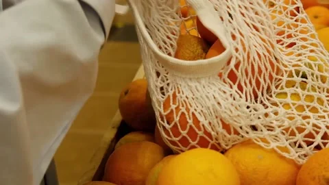 Female hands is picking, choosing oranges, folding in white mesh bag Stock Footage 155288806