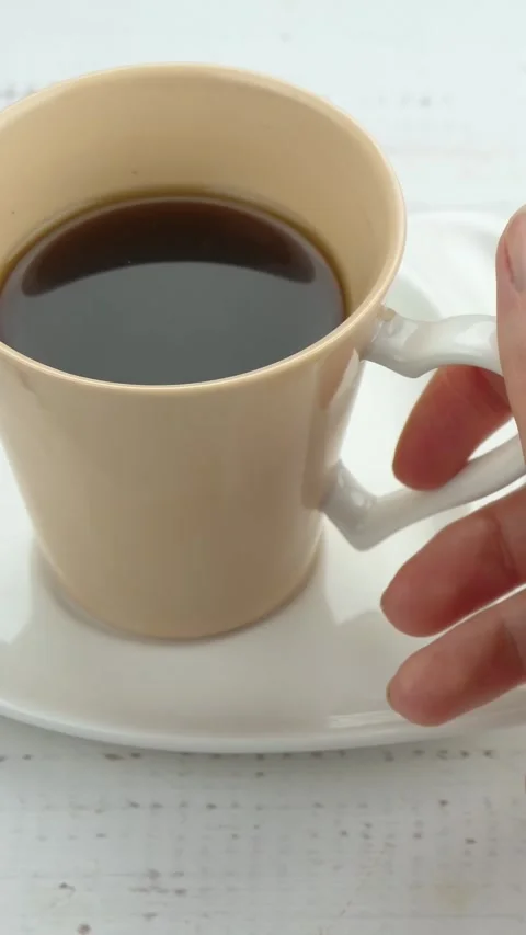 Female hands picking up coffee cup from white table. Warm beverage creates cozy Stock Footage 344523140
