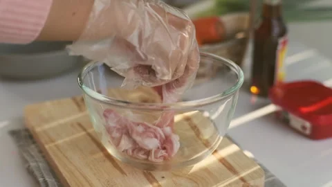 Female hands in a plastic glove picks up a sliced pork belly into a bowl. Stock Footage 242549444